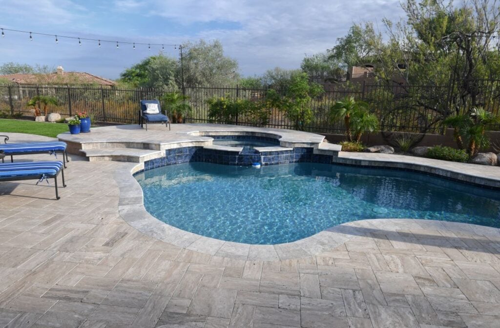 A desert landscaped backyard in Arizona featuring a travertine tiled pool deck