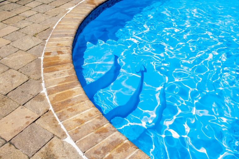 blue water in-ground pool with steps into the water from a brick platform indoors or outdoors